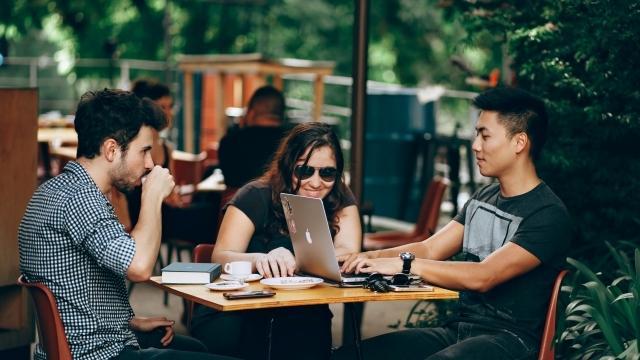 Three young people sitting at a cafe working on a laptop
