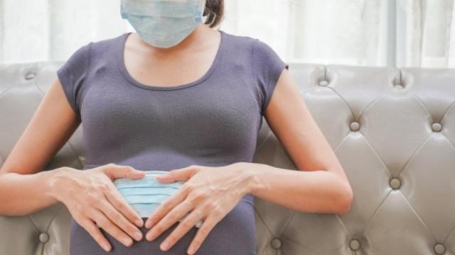 A pregnant woman wears a surgical mask to protect a COVID-19 (Coronavirus) and PM 2.5 and show a surgical mask on the abdomen to prevent infection to the fetus.