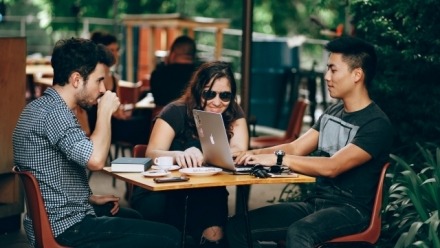 Three young people sitting at a cafe working on a laptop 